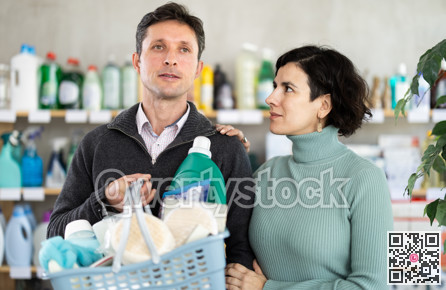 Man buyer and wife with filled basket wanders around store, looking at display cases.