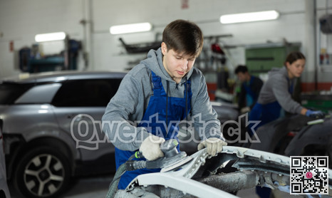 Young man auto mechanic polishes body parts by car buffer polisher machine tool