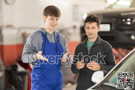 Young man car mechanic talks with man client in workshop and takes order.