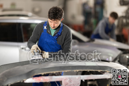 Car bumper repair in car service - professional car painter polishes and prepares bumper before painting