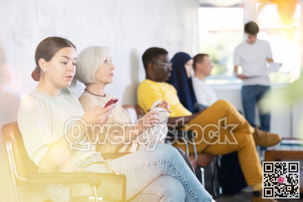 Positive young girl sitting with smartphone in lobby of medical clinic