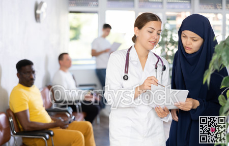 Young female doctor showing papers to Muslim woman in lobby of clinic