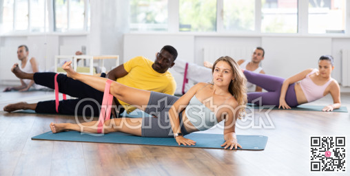 Pilates class - group of people of different nationalities doing leg stretches using resistance bands in gym