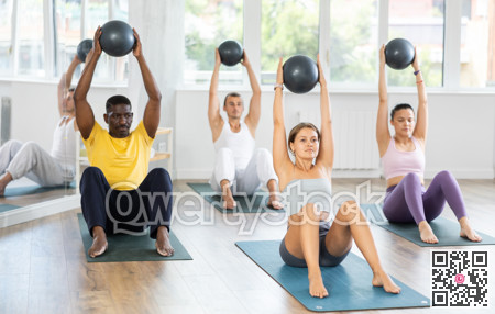 Pilates class in multi-ethnic group - men and women hold the ball above their heads and do bends