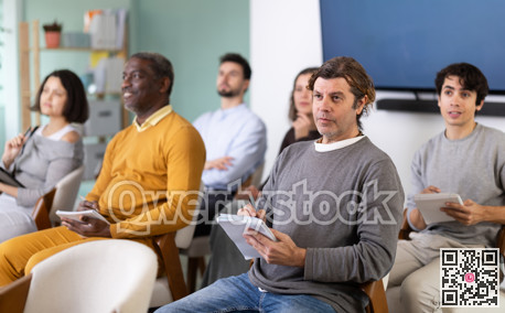 Students of different ages listen attentively to teacher and take notes in notebooks during a lecture at the learning center. Language course