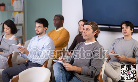 Students of different ages listen attentively to teacher and take notes in notebooks during a lecture at the learning center. Language course