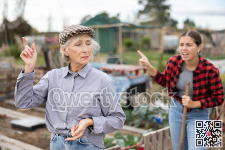 Two upset young and old female neighbors disagree with each other while digging garden on smallholding in autumn