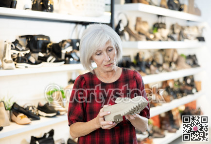 Mature woman buyer looks at footwear from new collection and picks up new pair of moccasins shoes