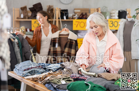 Senior woman customer examine and choose sweater in store. Other buyer in background, crowded shop