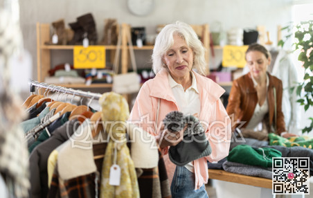 Senior woman customer examine and choose hat. Other buyer in background, crowded shop