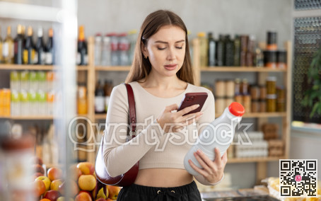 Female buyer checks suitability - scans QR code on bottle of milk label in grocery store