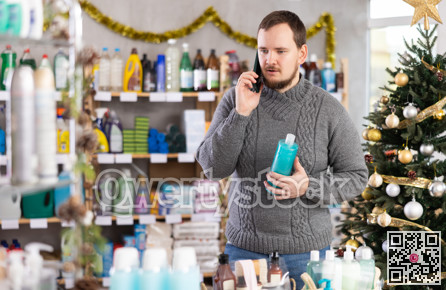 While shopping, man talks on phone, walks along windows and consults with wife about purchases