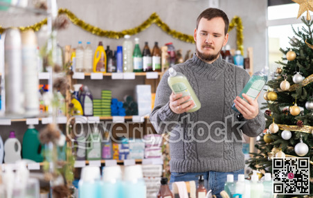 Middle-aged guy choosing dishwashing liquid in store with New Year decoration