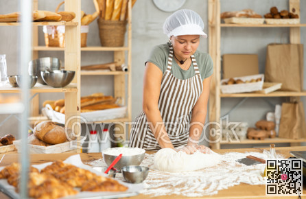 Young smiling female baker preparing raw yeast dough on kitchen table in bakery