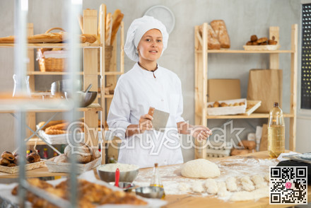 Female baker in uniform cutting raw dough with knife to make croissants or buns