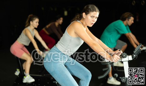 Sportive young girl doing spin bike exercises in well-equipped gym