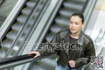 Positive young woman in black leather jacket riding up an escalator at metro station