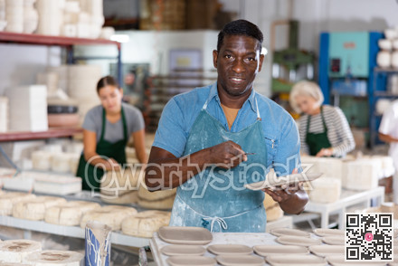 Positive man potter with new crafted crockry in workshop