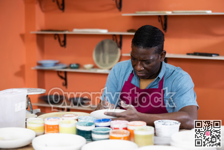 Male craftsman painting clay plates acrylic paints in art studio