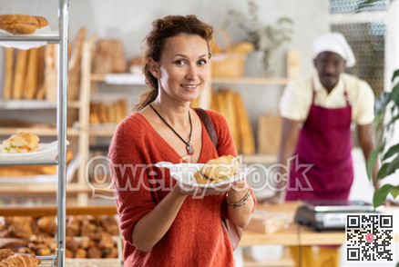 Happy female customer tries delicious bocadillo in bakery interior