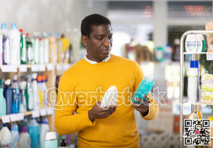 Male buyer chooses shampoo or shower gel in household goods department of supermarket