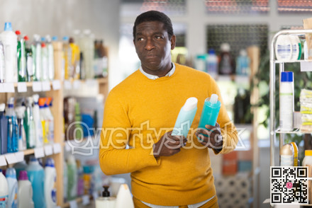 Male buyer chooses shampoo or shower gel in household goods department of supermarket