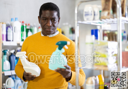 Before buying in household shop, African male customer choose glass cleaner spray