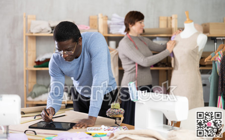 Fashion designer sketching garment on tablet while colleague working with mannequin