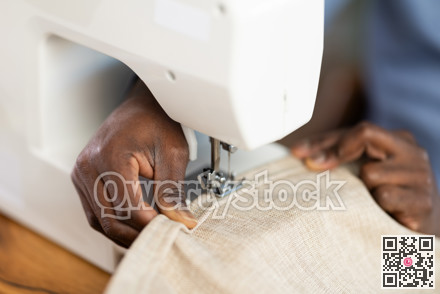 African American man tailor sews clothes in sewing machine, close up