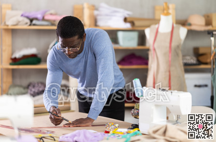 Middle-aged male dressmaker sketching clothing pattern in sewing workshop