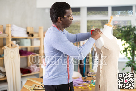African American man tailor connects parts of dress on mannequin.