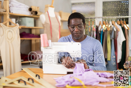African American man tailor sews clothes in sewing machine.