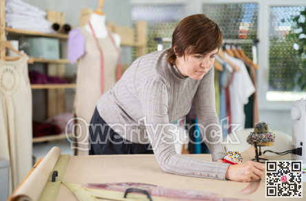 Female dressmaker draws sketch of future clothing on paper using patterns in sewing workshop