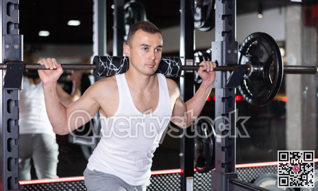 Sporty man performing set of exercises with barbell during intense workout