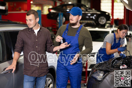 Happy man next to car being repaired. Auto mechanic gives man keys to his car
