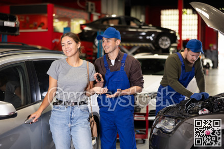 Kind car mechanic handing over the keys of car to glad female client in auto shop