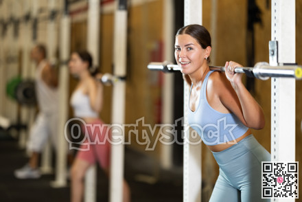Focused girl in activewear exercising with barbell during group workout in gym
