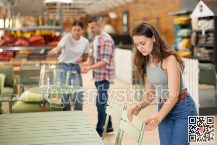 Young female shopper choosing chairs in garden furniture store