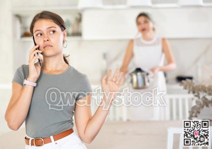 Upset daughter is sitting at table. Mom yells at her daughter in background