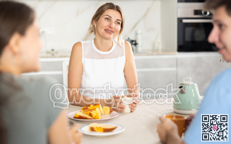 Cheerful woman receiving guests over cup of tea at home kitchen table