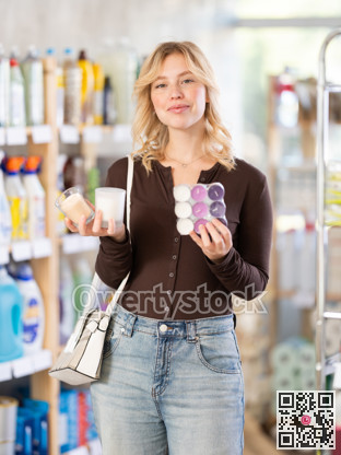 Girl housewife in household store examines goods, chooses candle
