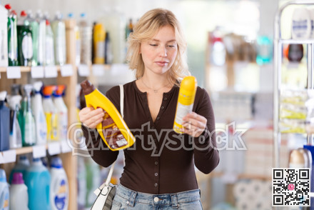 Girl housewife in household store examines goods, chooses liquid furniture polish