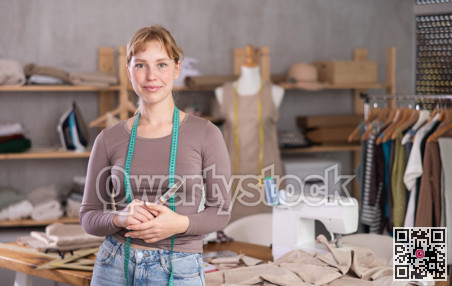 Smiling young female dressmaker posing in sewing studio