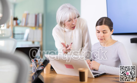 Elderly woman scolding adult female colleague working on laptop
