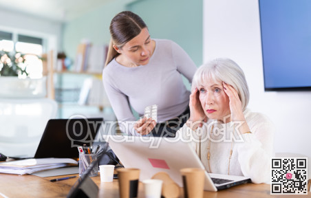 Elderly businesswoman suffers from a headache. Colleague offers her headache pills.