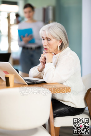 Elderly woman working on laptop adult colleague shows document