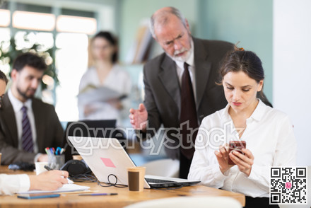 Strict mature man boss scolding girl office worker for scrolling social media on smartphone during work hours in office