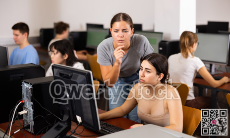 Focused young woman student working with her female friend in computer class, using pc in library