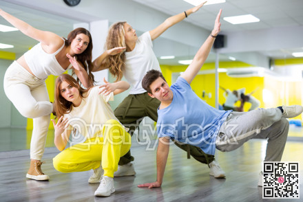 Teenage girls and a boy performing breakdance poses in dance hall