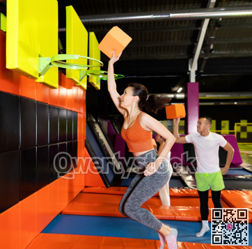 Athletic people throw ball into basketball basket while jumping on trampolines at an entertainment center